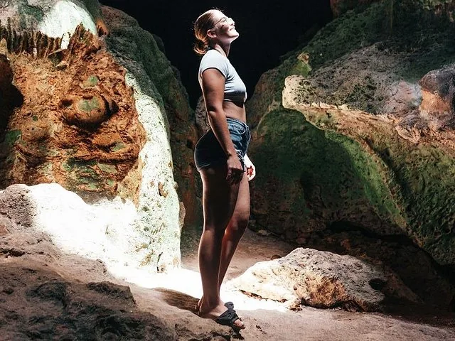 Une femme debout dans une grotte, levant les yeux vers les formations rocheuses éclairées par le soleil.