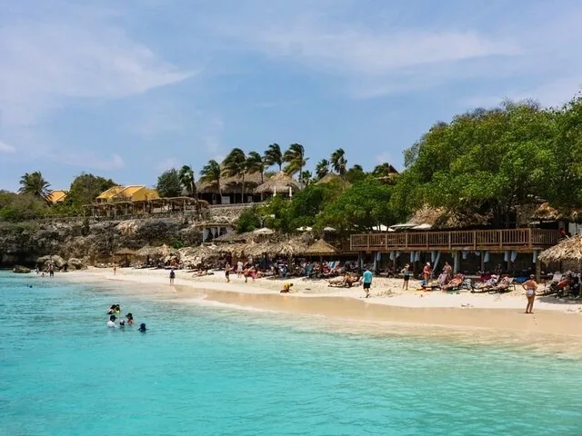 Personas relajándose en una playa de arena con agua turquesa y palmeras